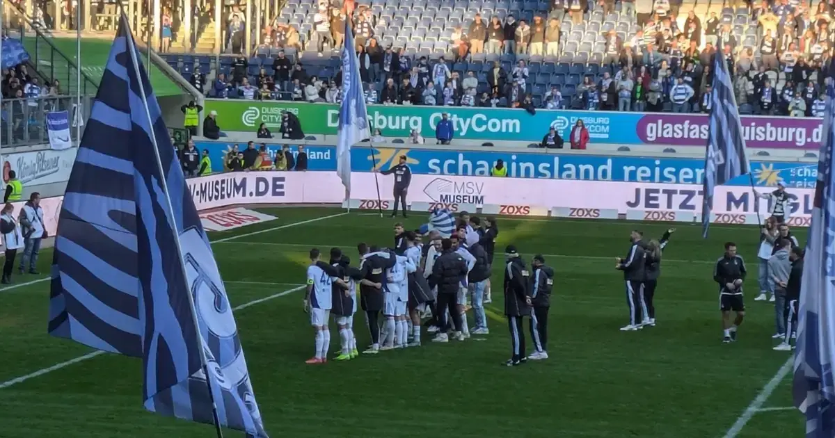 Erfolg: Spieler des MSV Duisburg versammeln sich im Stadion während der Halbzeit, große MSV-Fahnen im Vordergrund.