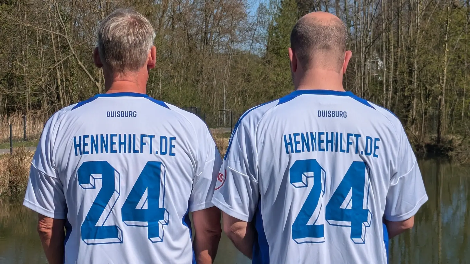 Zwei Männer mit MSV-Trikots und der Aufschrift „HENNEHILFT.DE 24“ von hinten.